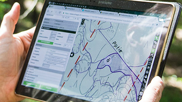 Eine Person hält ein Tablet in der Hand, auf dem eine digitale Karte mit topografischen Linien und Wegen angezeigt wird.
