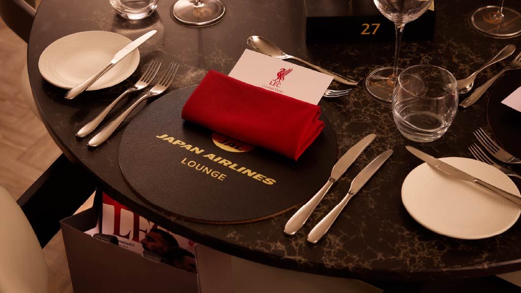 Elegant dining table set for the Japan Airlines Lounge with LFC menu card, red napkin, silverware and glassware on dark marble.