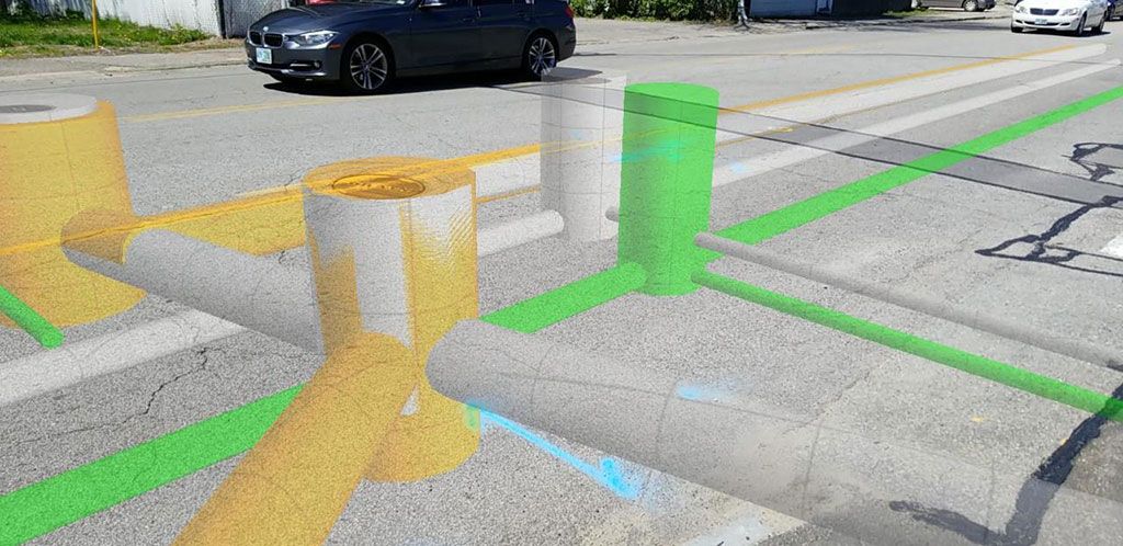 Augmented reality overlay shows underground utility pipes in yellow, green, and blue on a street.