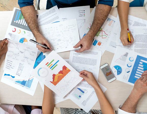 Team collaborates around a table filled with charts, graphs, and documents.
