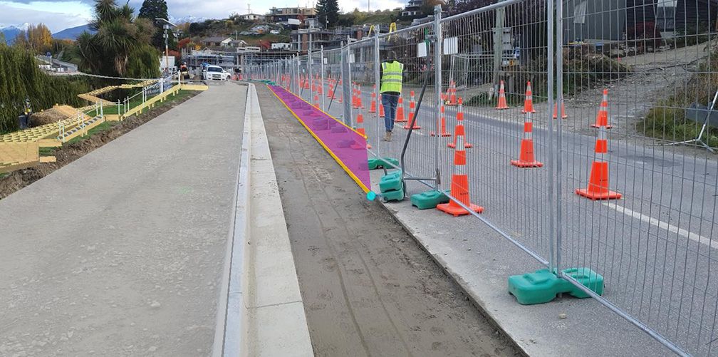 Construction site with safety fencing and orange traffic cones along a paved path.