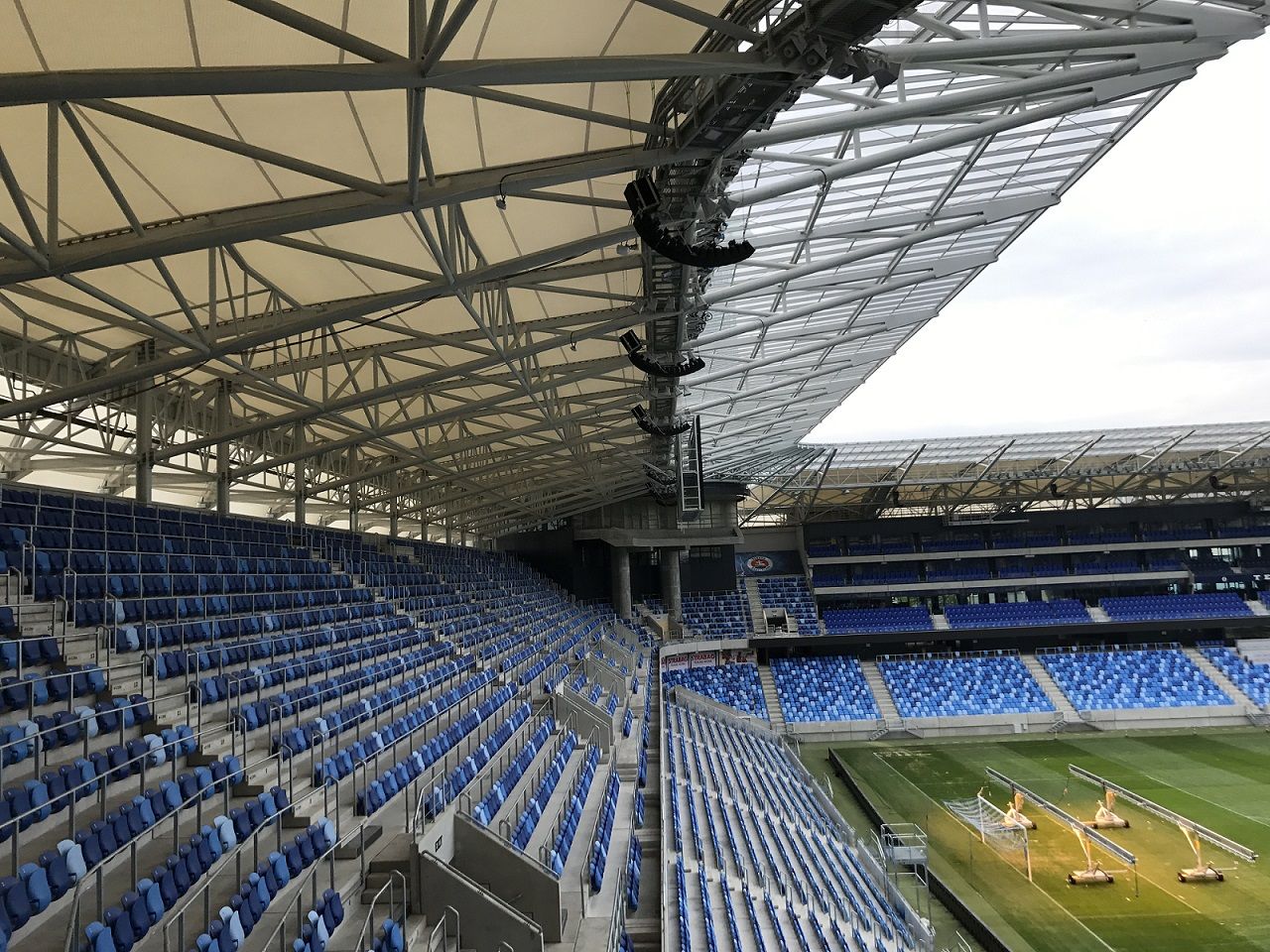 Empty stadium seats with a view of the soccer field and roof structure.