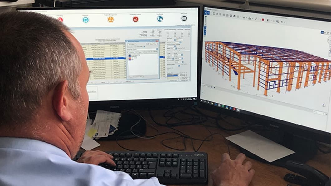 Waring Buildings employee sat at computer, Tekla PowerFab shown on two computer monitors