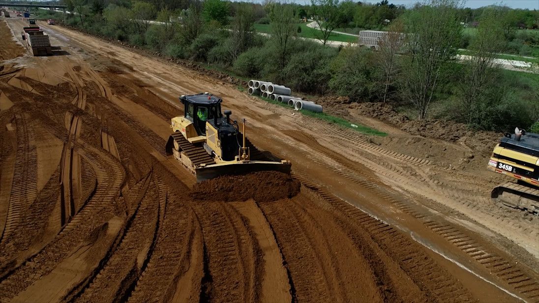 A bulldozer levels earth at a construction site, leaving behind tire tracks.