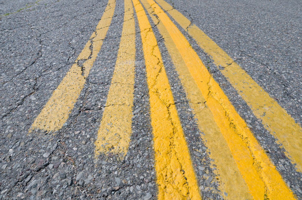 Close-up of double yellow lines painted on a cracked asphalt road.