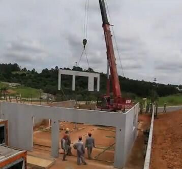 A large red crane lifts a precast concrete wall panel into place at a construction site, where workers are assembling a new building.