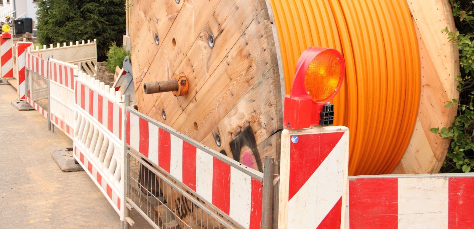 Construction site with large wooden spool of orange conduit, safety barriers, and warning lights.