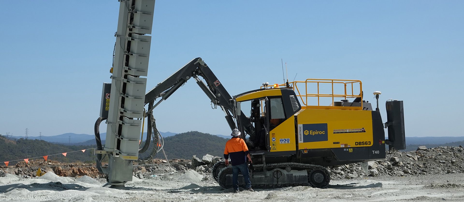 Side view of a red drill rig positioned on cleared rocky terrain in an open-pit quarry.