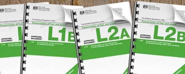 Four spiral-bound UK Building Regulations documents labeled L1A, L1B, L2A, and L2B with green covers on wooden surface.