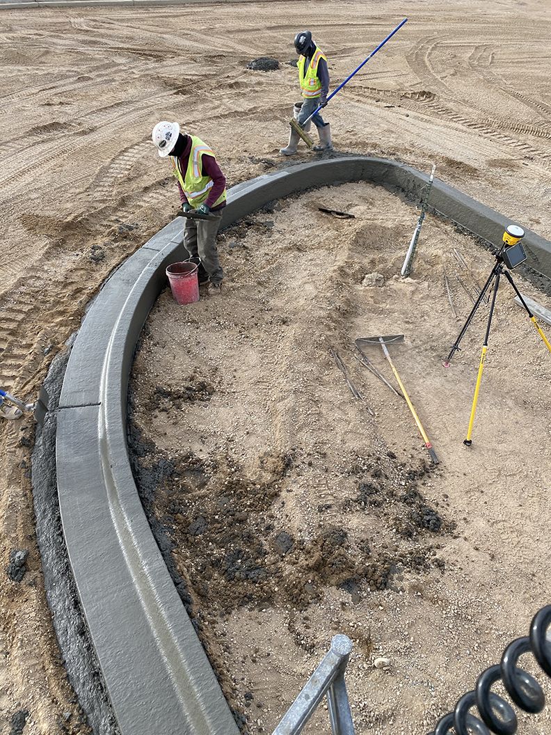 Workers in safety vests and hard hats pour and shape concrete for a new curb at a construction site.