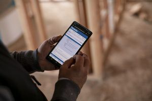 Hands holding a smartphone displaying a digital document, with a construction site in the background.