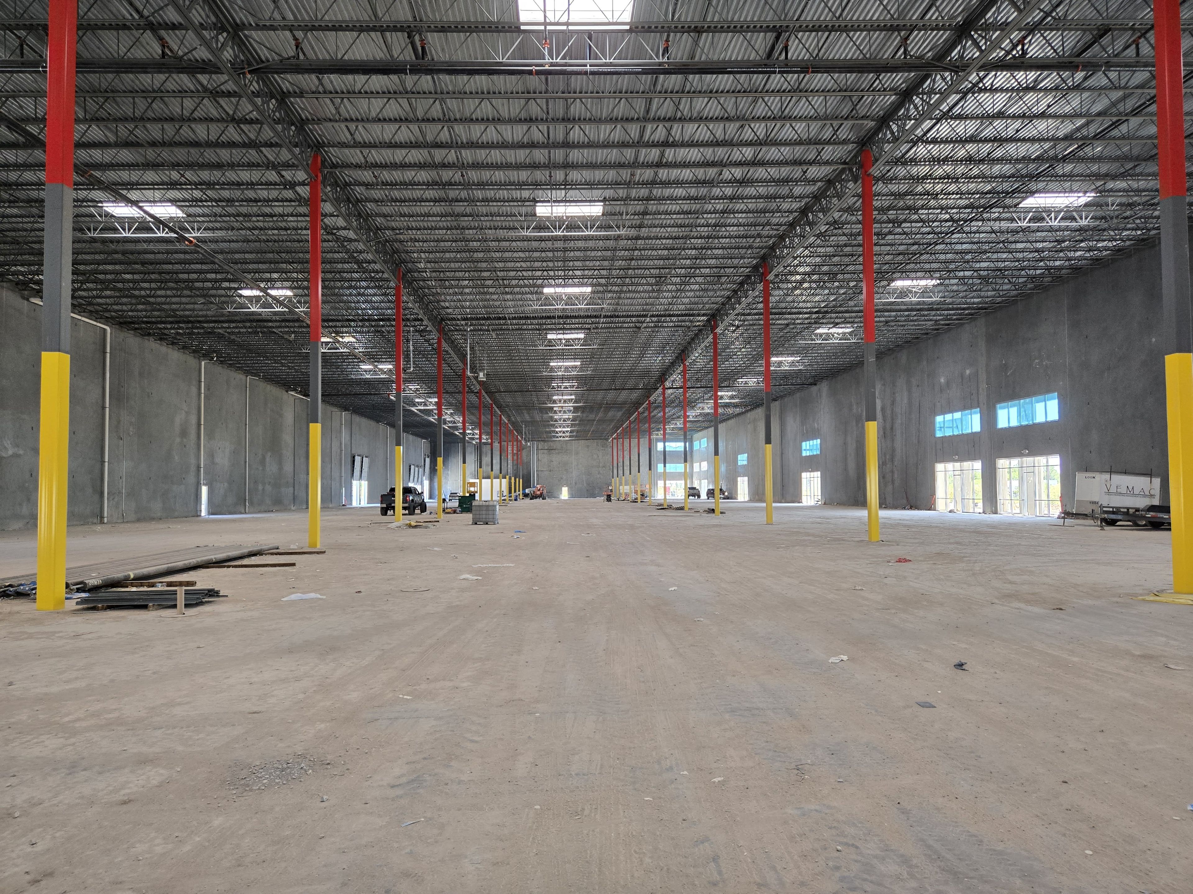 Interior of a large, empty warehouse with concrete walls, metal ceiling, and red and yellow support columns.