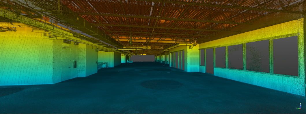 Empty industrial interior space with colorful gradient lighting in blue, green, and yellow tones illuminating the walls.