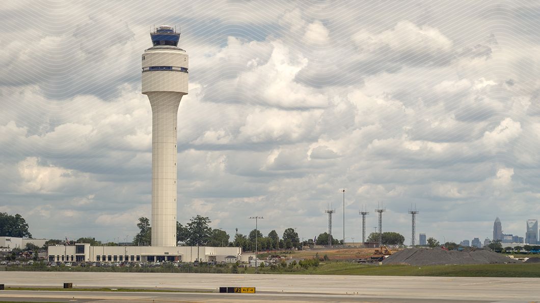 CLT 370-ft ATC tower. Construction site with earthwork, aggregate, yellow excavator near Charlotte skyline.