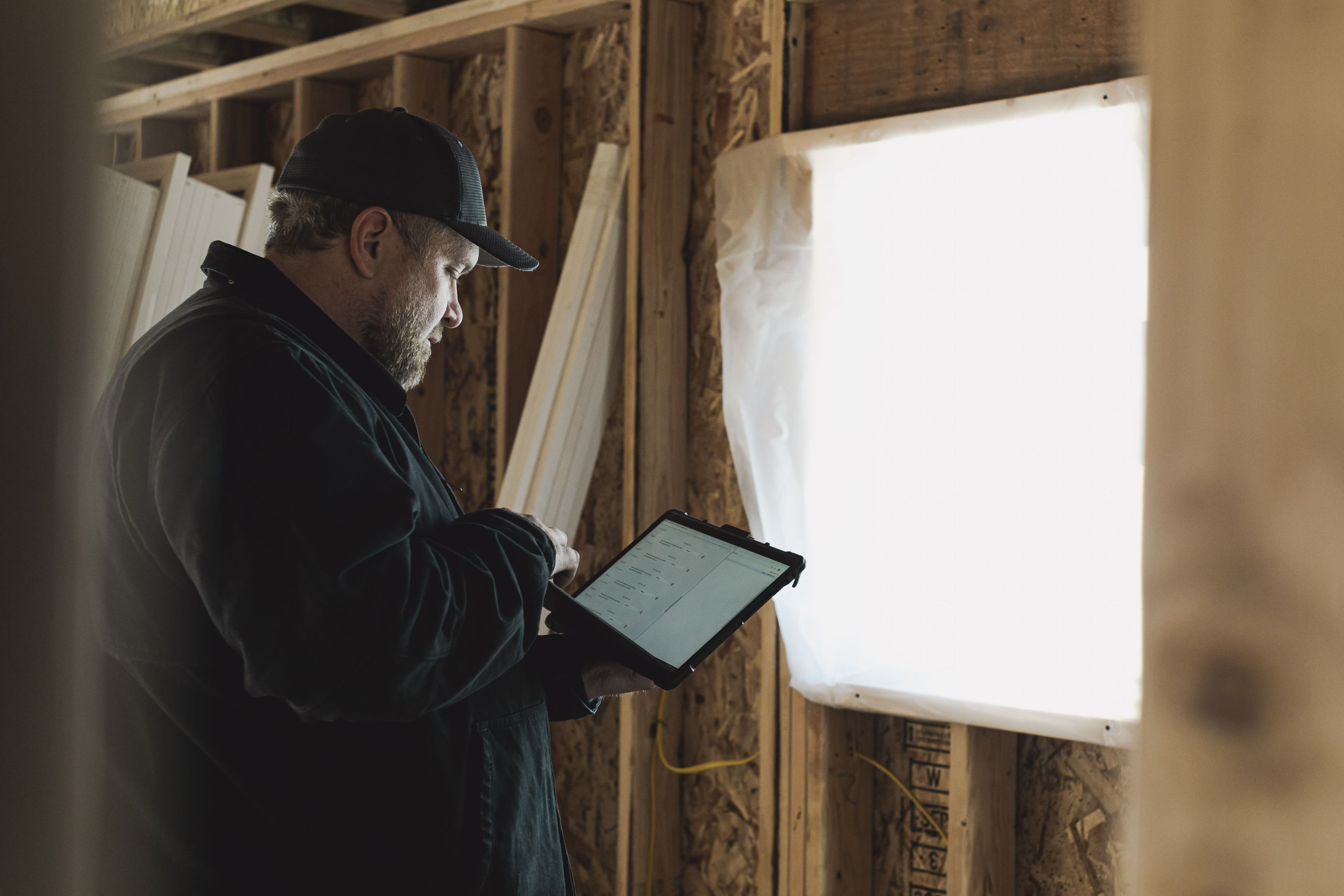 Construction worker in a hard hat reviewing plans on a tablet at a job site.