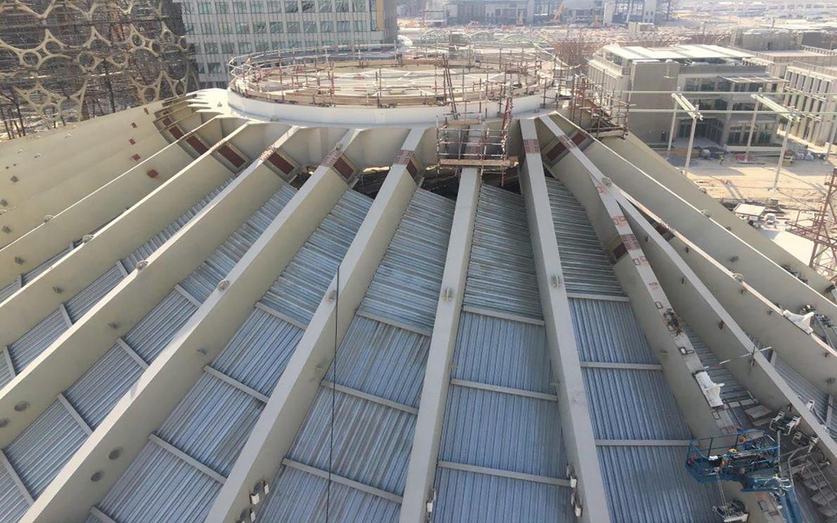 Construction of a large, geodesic-style dome roof with exposed steel beams and corrugated metal sheeting.