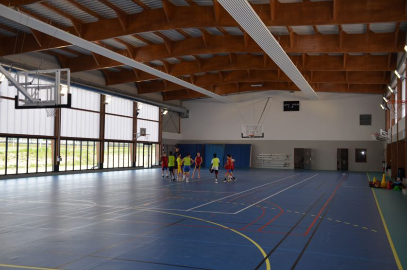 A group of young children are playing a game of basketball on a blue court in a large, well-lit gymnasium.