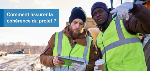 Two construction workers in high-visibility vests look at a tablet.