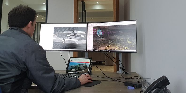 Architect works on dual monitors displaying 3D models and site scan data.