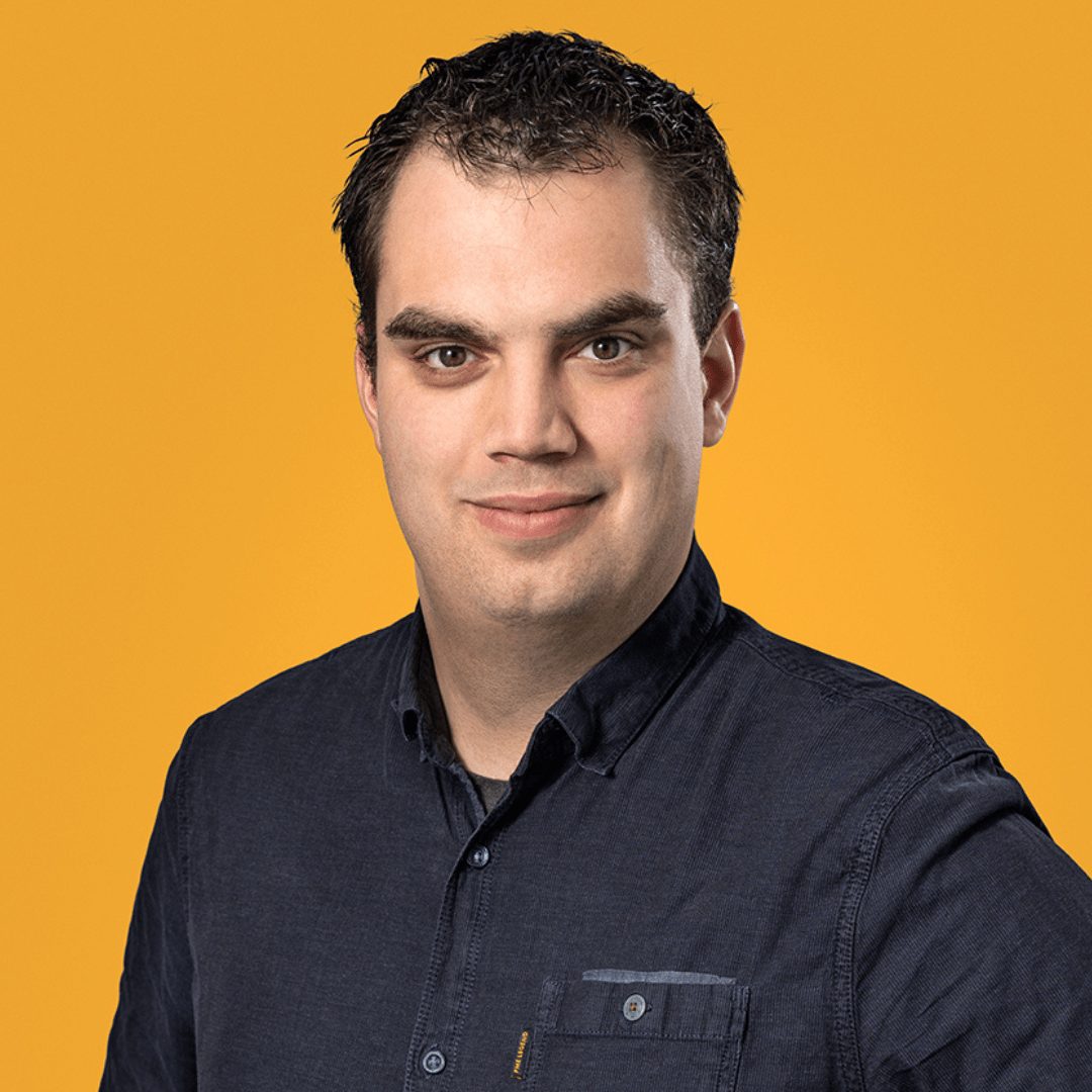 Roger Fuchs, a man with dark hair and a dark blue shirt, smiles against a yellow background.