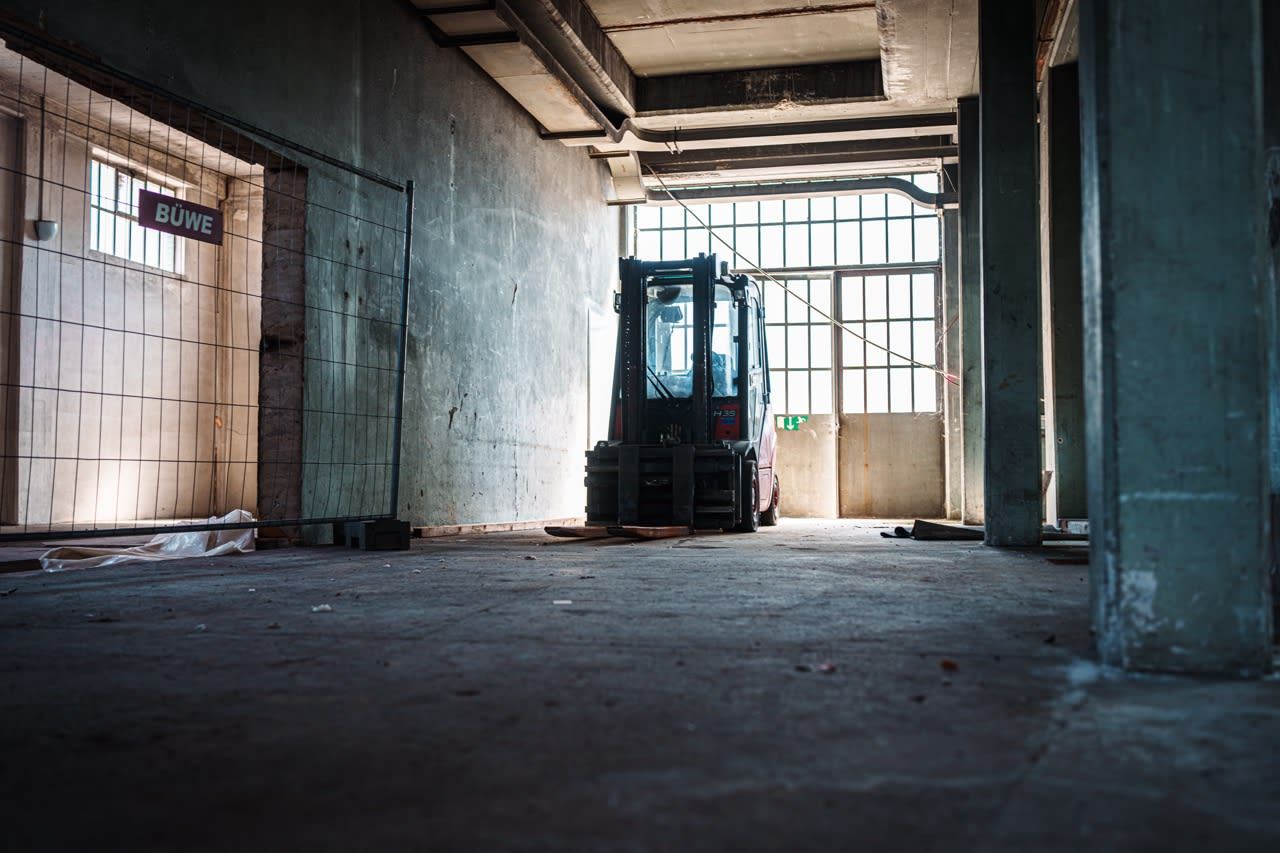 Forklift in a large, empty industrial space with concrete walls and large windows.