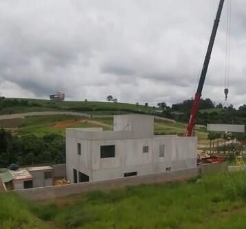 A concrete house is under construction on a grassy hill, with a large crane extending over the scene.