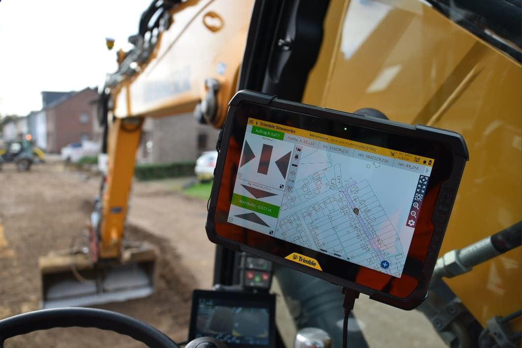 A Trimble Siteworks tablet in an excavator cabin shows a digital map and excavation data, with a construction site outside.