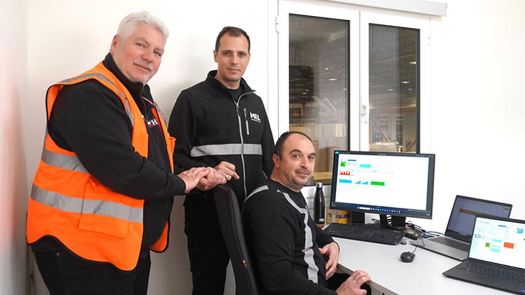 Three male engineers from the MEL Paper posing in an office at a workstation showing process data on multiple computers.