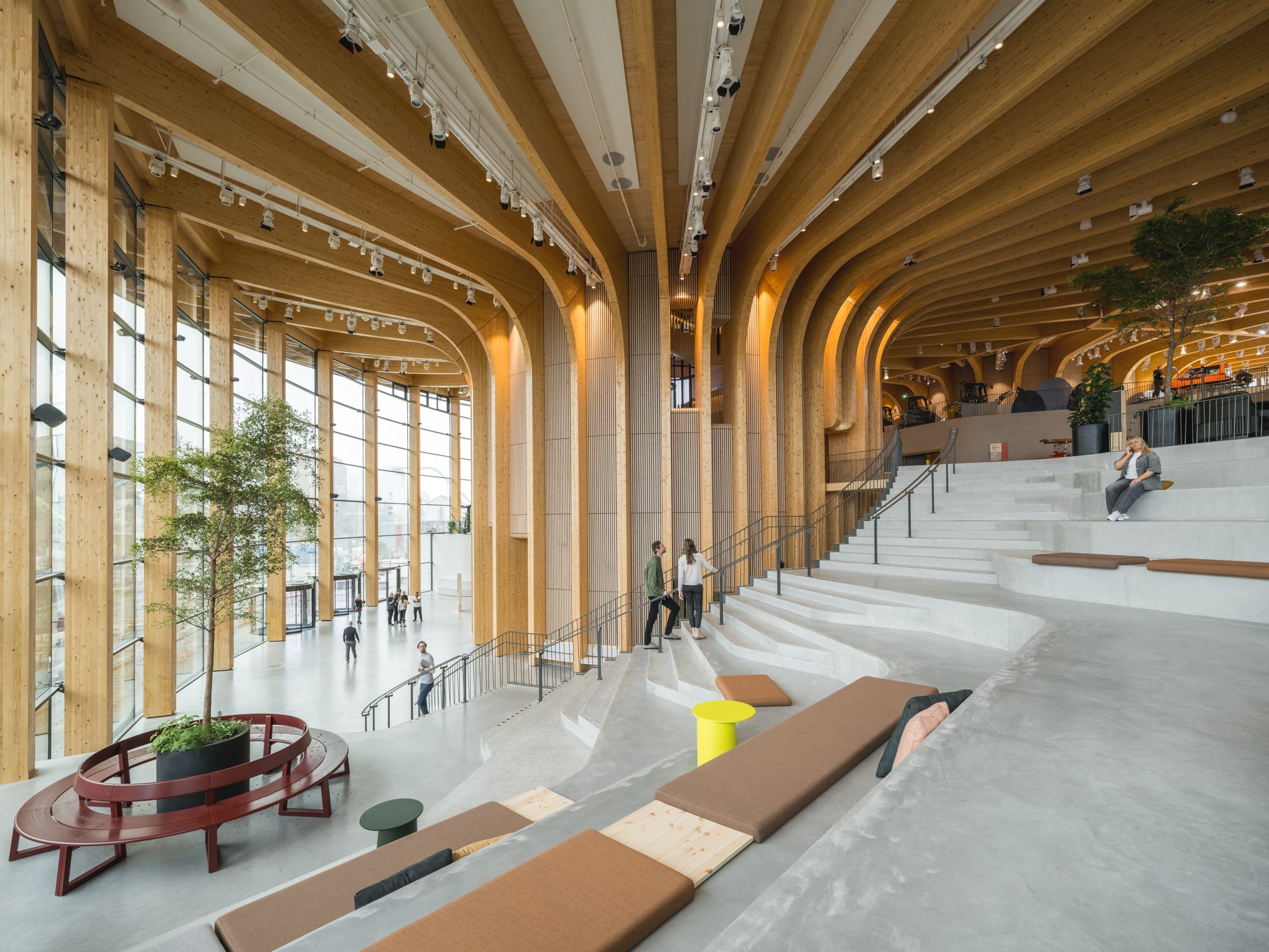 Interior view of the Grand Stairway at World of Volvo, featuring a dramatic curved wooden ceiling, tall windows and tiered concrete seating.