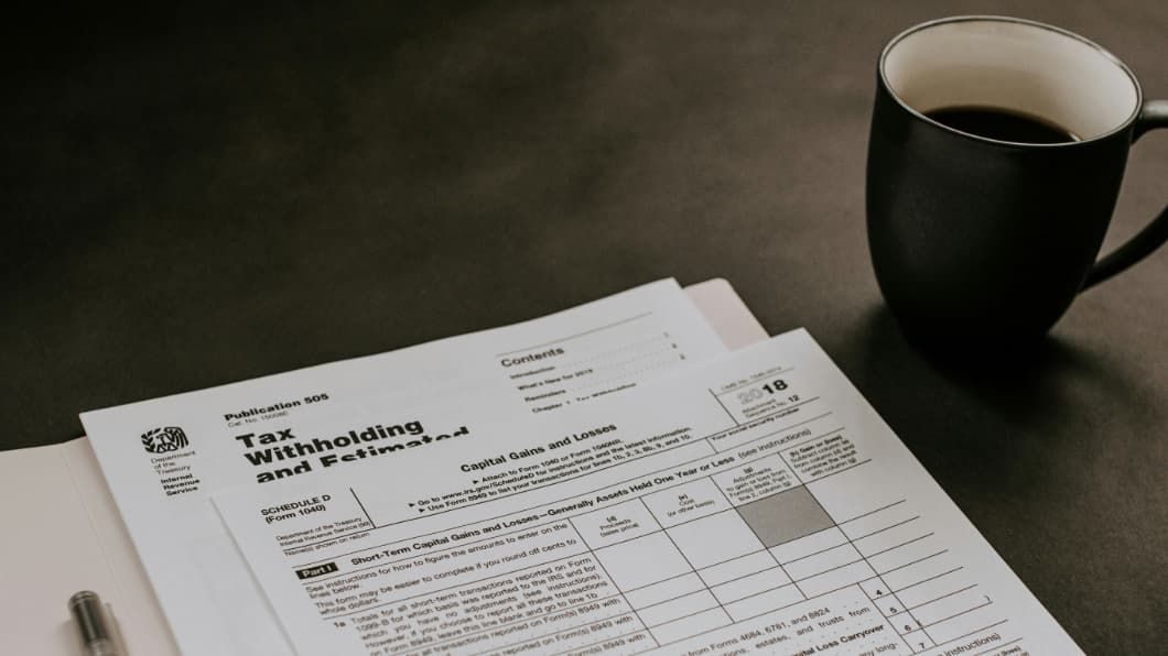 Close-up of IRS Publication 505 and Schedule D (Form 1040) for Capital Gains and Losses with a pen and coffee.
