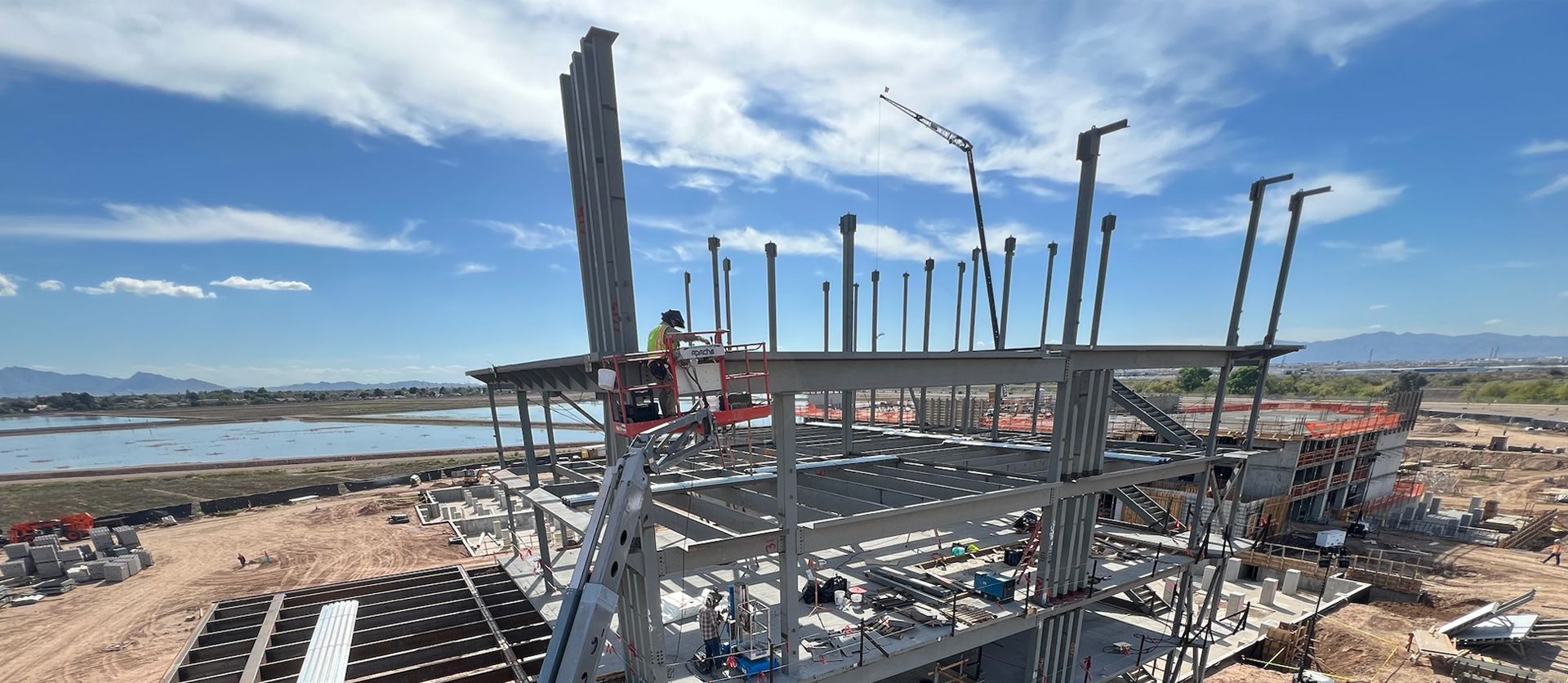 Fuze ballpark construction site featuring a multi-story steel frame building under a bright sky, with a crane and cherry picker in use.
