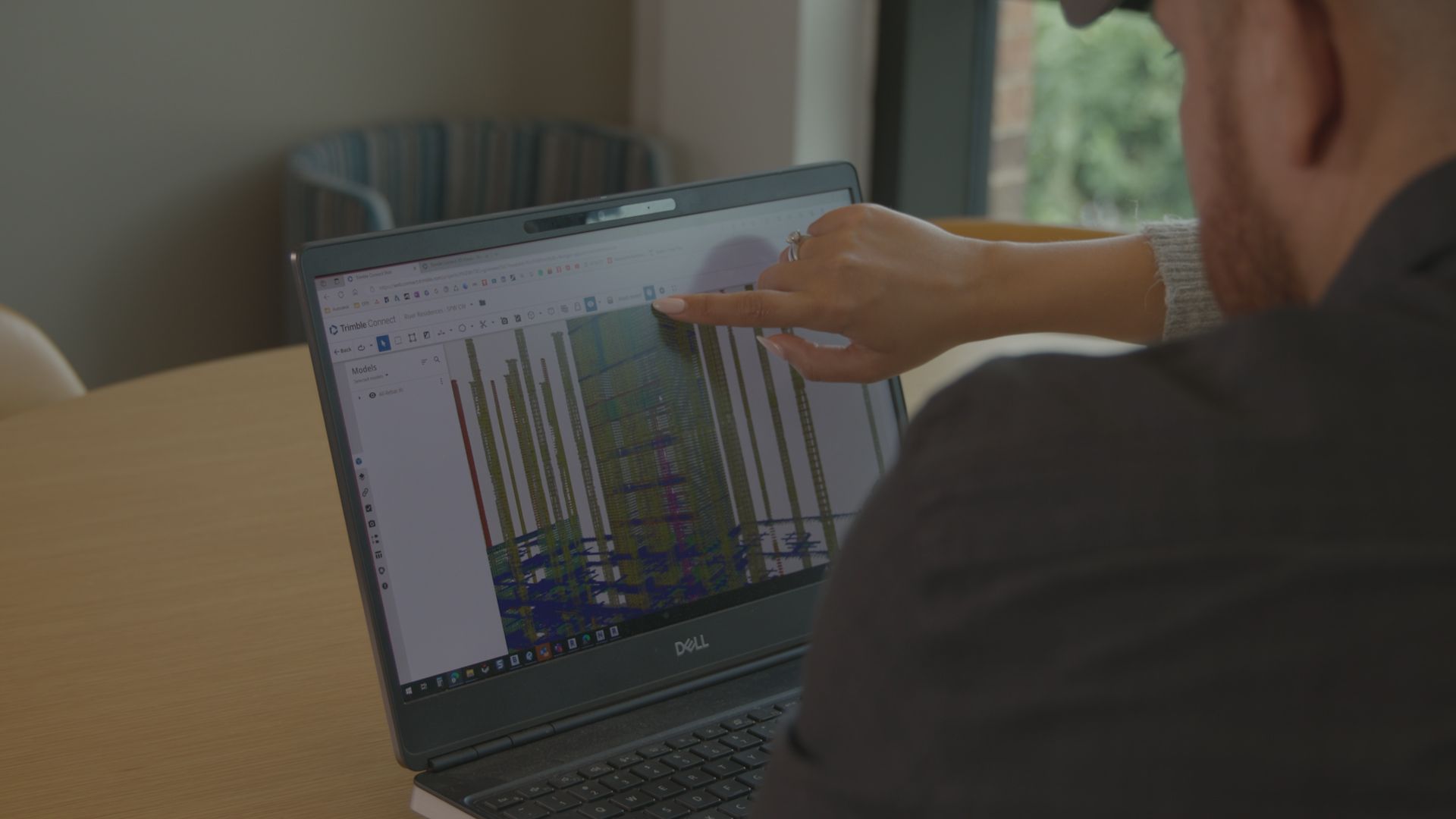 Two people look at a laptop showing a 3D model.