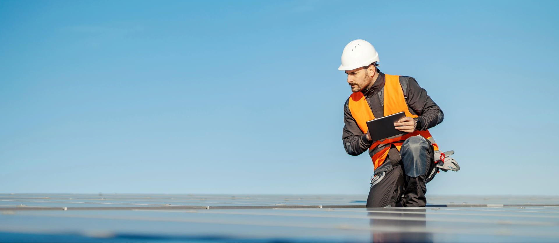 Technicus in veiligheidsvest gebruikt een tablet op een dak met zonnepanelen.