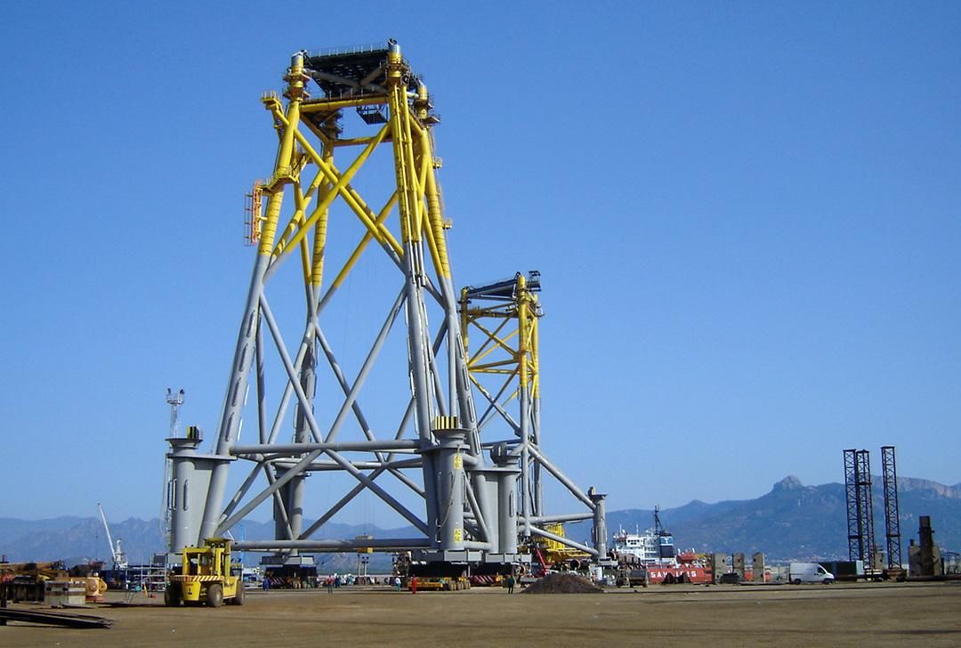 A large yellow and gray offshore jacket structure is being prepared for loadout on a clear day.