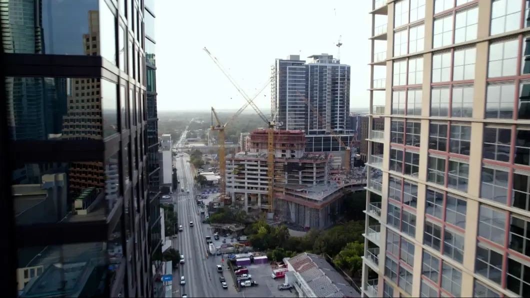 Cityscape with skyscrapers and construction cranes under a cloudy sky.