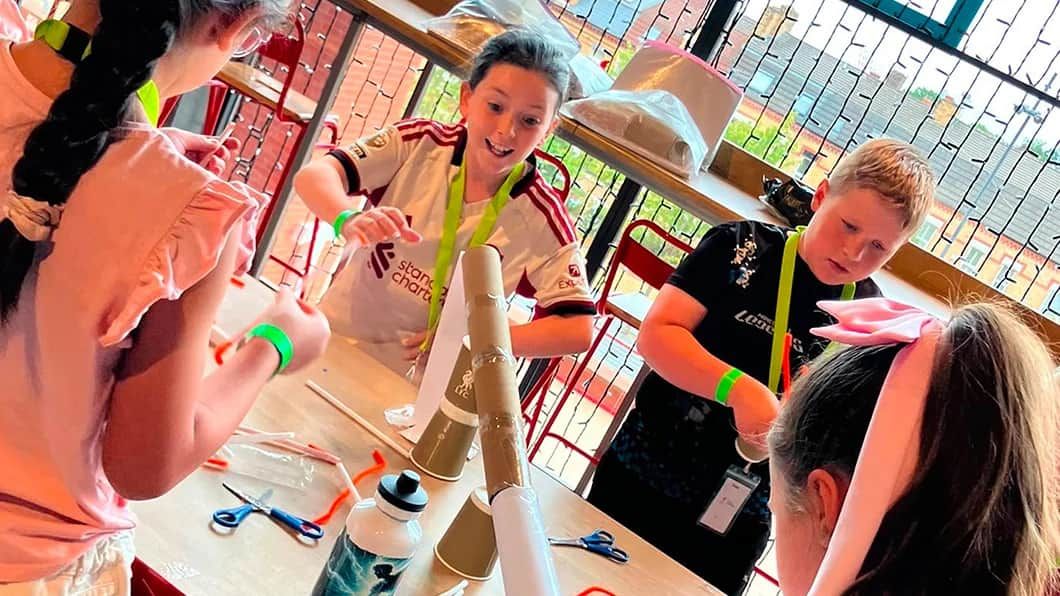 Smiling children collaborate to build a cardboard tower during a hands-on STEM activity.