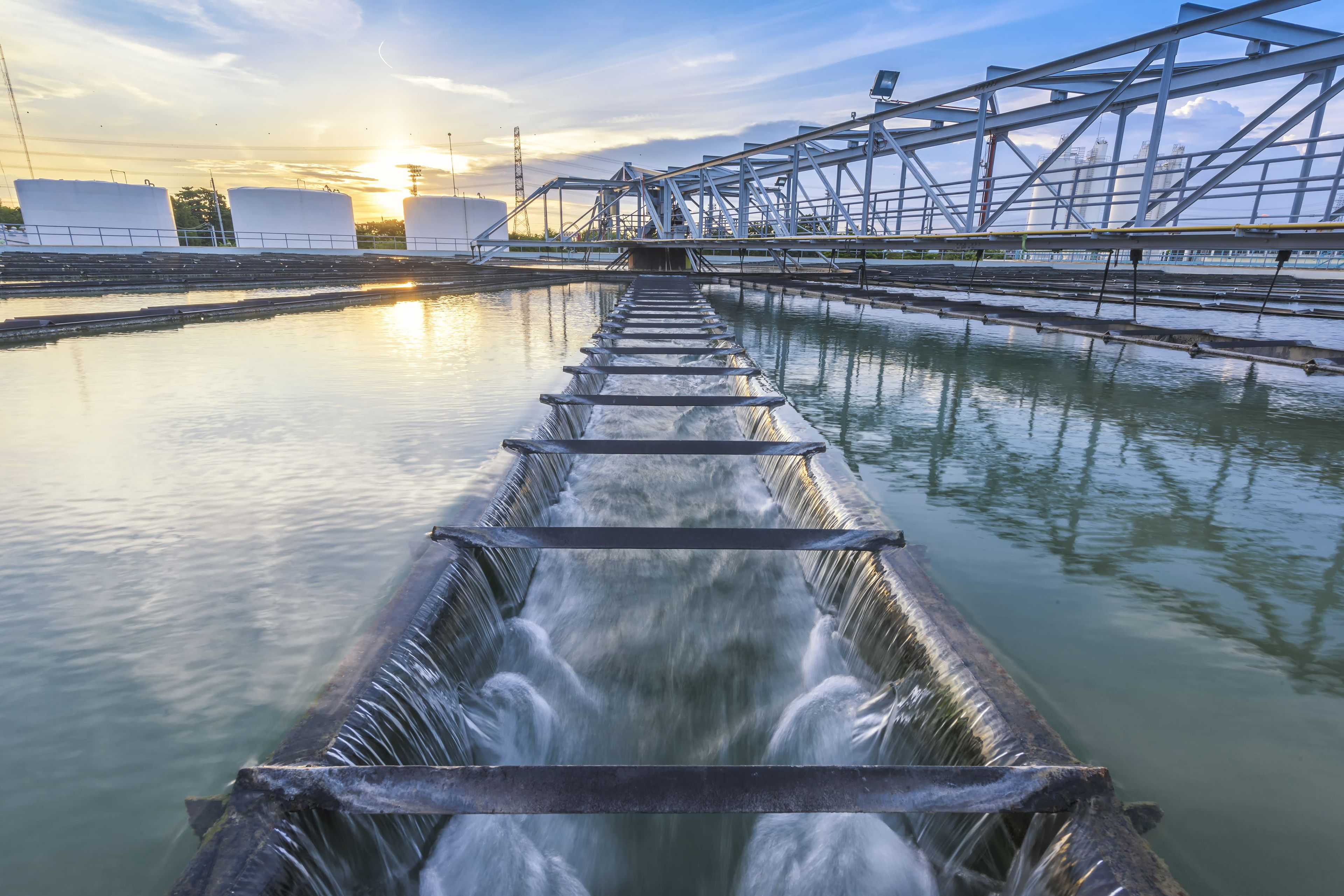 Water treatment facility with cascading water flow and industrial infrastructure under a sunset sky.