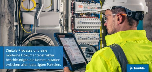 A worker in a hard hat and safety vest uses a tablet in front of an electrical panel.