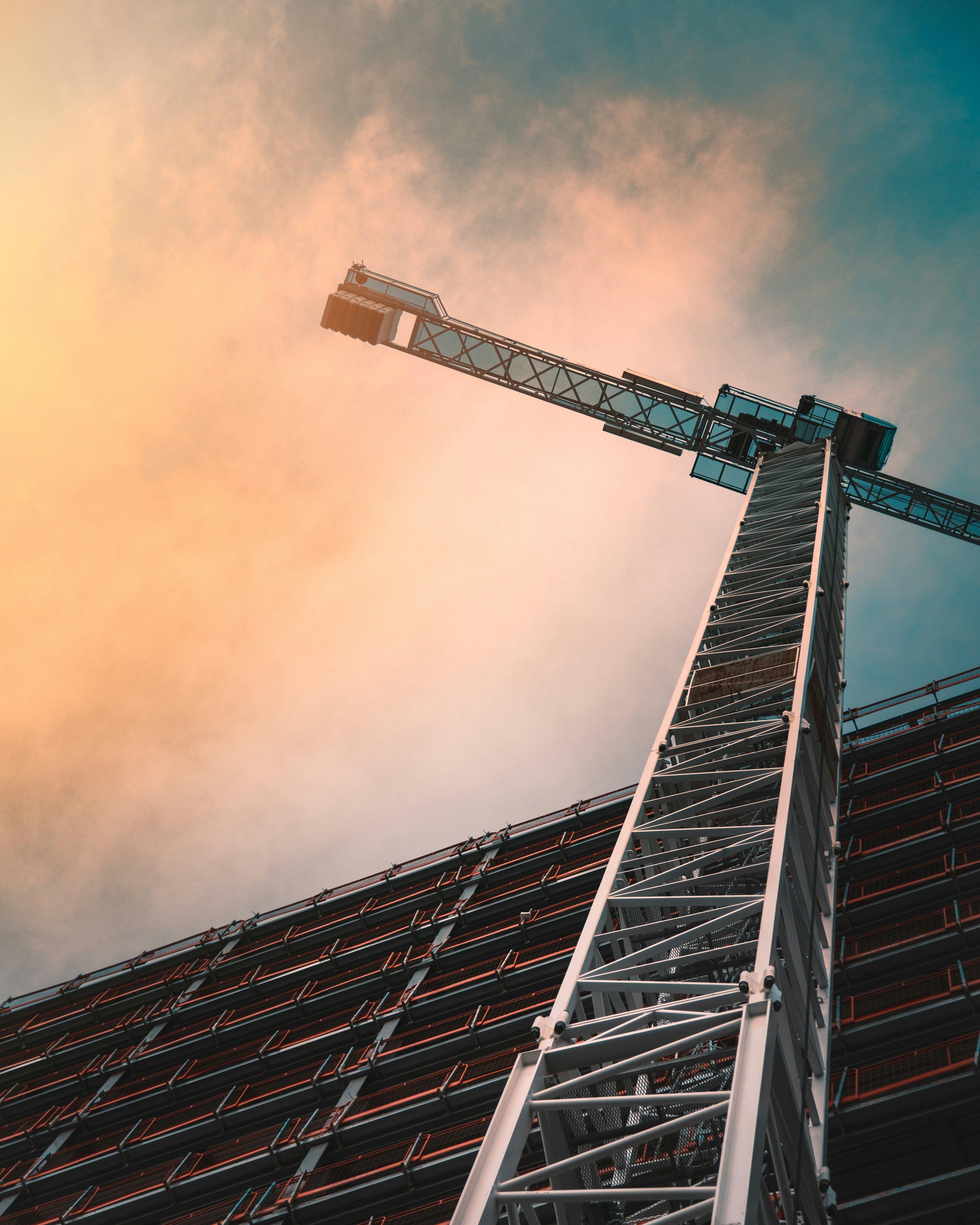 A close-up, low-angle shot shows a tall construction crane against a dramatic sky.