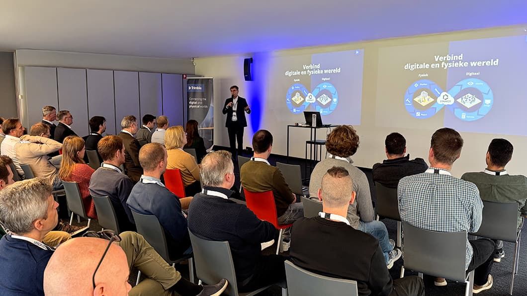 Een publiek kijkt toe terwijl een spreker een "Digital and Physical World"-diagram presenteert op een Trimble-conferentie.