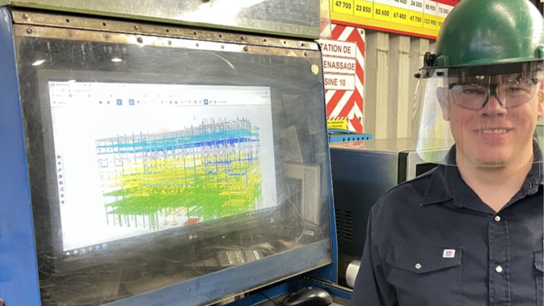 Person on a steel shop floor standing next to a screen displaying a Trimble Connect project.