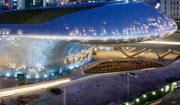 A futuristic building with a metallic, curved facade illuminated at night, with small lights scattered across its surface and along its base.