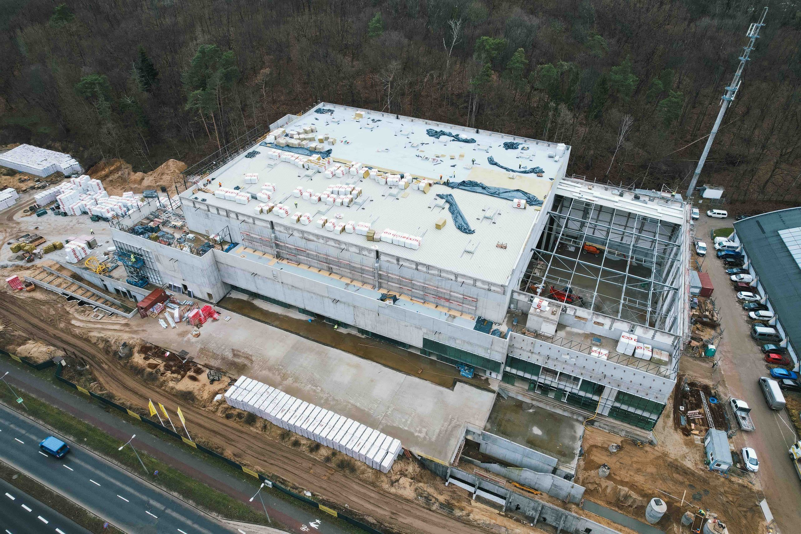 Aerial view of a large industrial building under construction, with exposed steel framework and concrete walls.