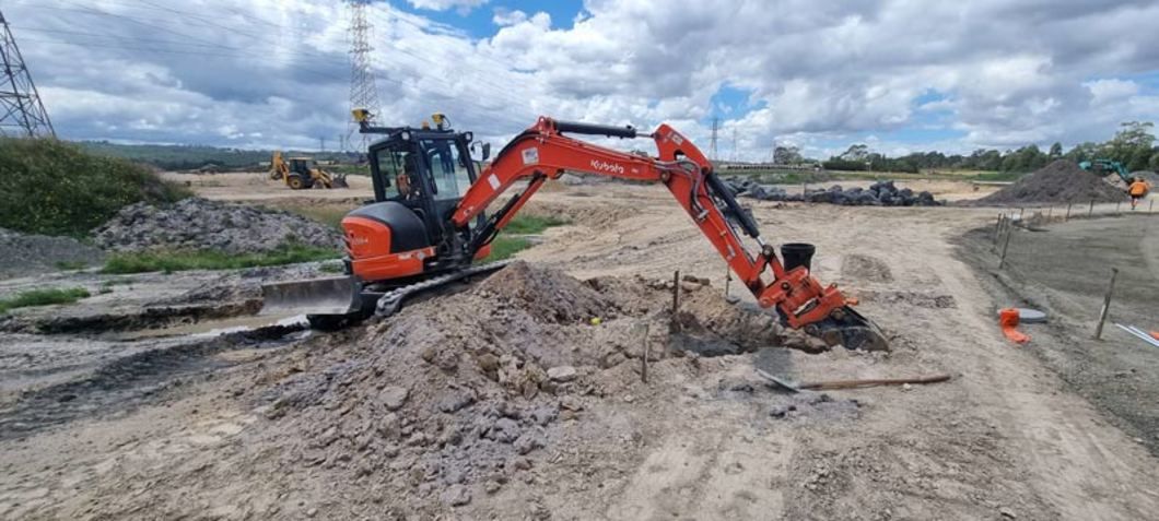 Orange excavator working on a construction site under a cloudy sky.