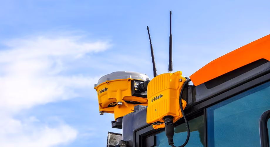 Close-up of a Trimble GPS receiver and communications device mounted on construction equipment under a blue sky.