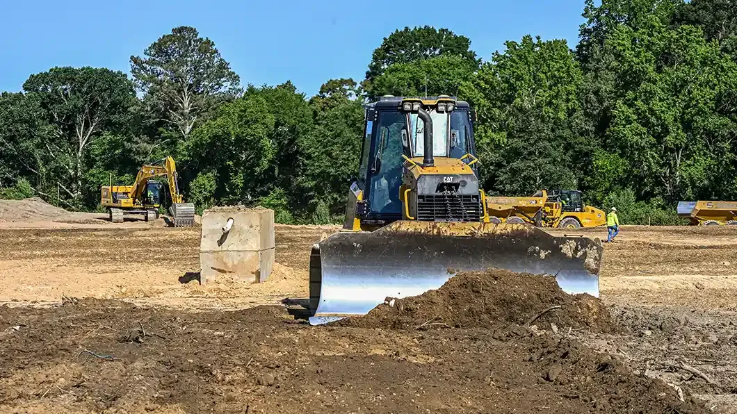 A bulldozer leveling dirt at a construction jobsite with an excavator in the background.