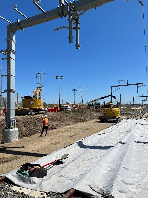 Construction of new overhead electrical lines for a railway with excavators and a worker on-site.