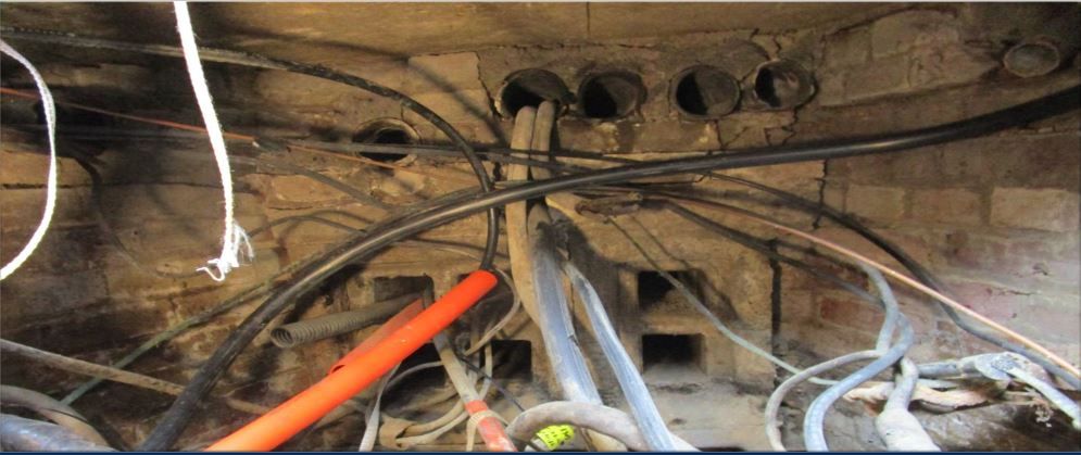 A chaotic tangle of electrical conduits and wires are routed through a brick wall.