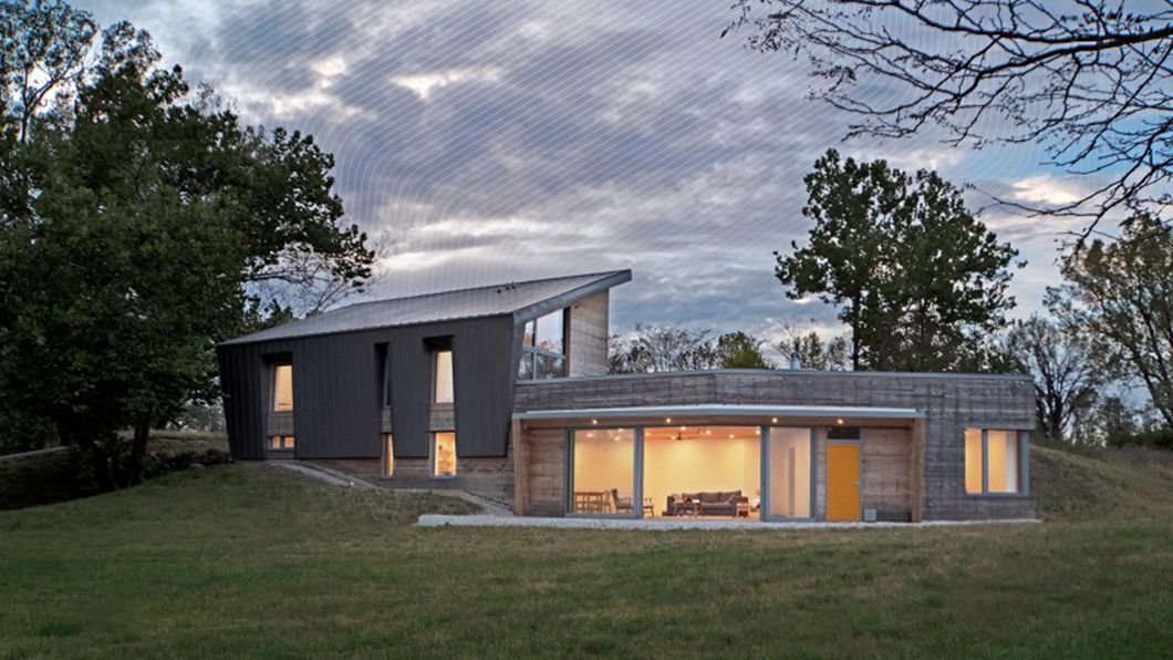 Modern multi-volume home: dark metal & weathered timber cladding, asymmetrical roof, large glazed sliding doors, yellow door, grassy site.
