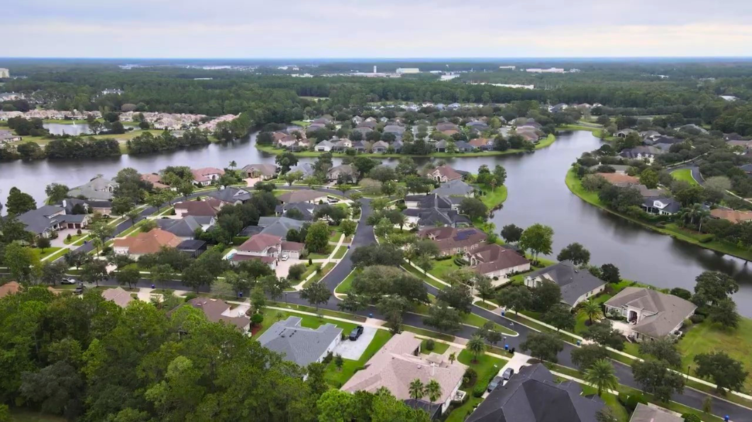 An aerial view of a suburban neighborhood in St. Johns County, Florida, with homes along winding streets and a calm river under an overcast sky.